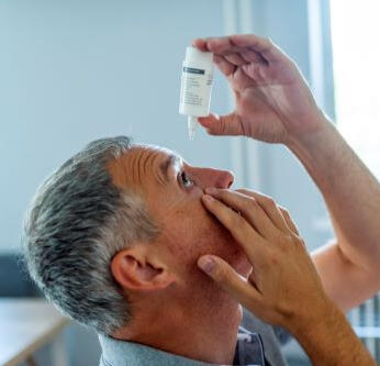 An older man is trying to put in some eye drops.