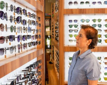 An older lady is looking at a wall of sunglasses frames with an intent expression on her face.